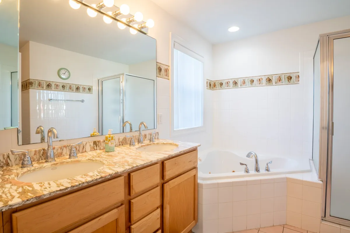 A bright ensuite bath with a double sink vanity, large mirror, bathtub, and glass shower enclosure. The space feels open and rejuvenating, perfect for self-care routines and unwinding after a long day.