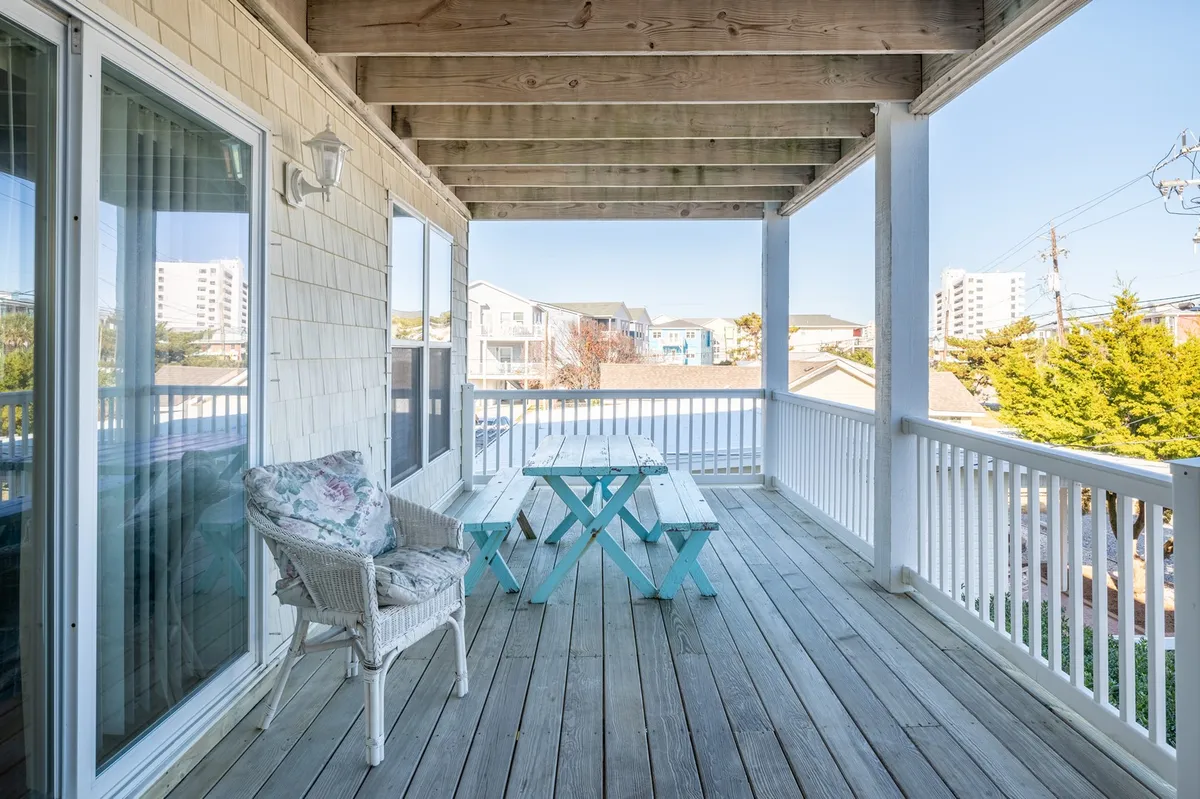A casual, inviting outdoor dining area with a wicker chair and table, framed by views of surrounding buildings. The atmosphere suggests a relaxed spot for breakfast or evening gatherings after fun-filled days on the beach or boardwalk.