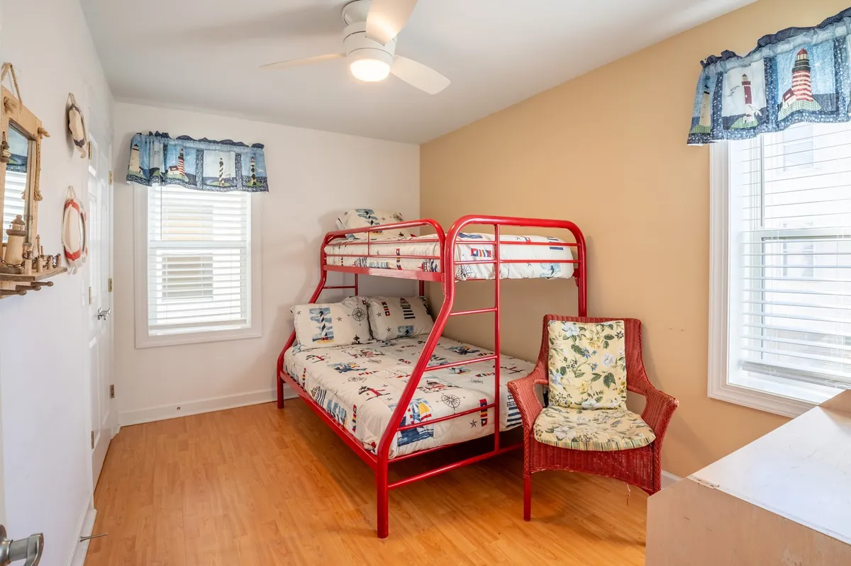 A playful bunk room featuring a bunk bed, accent chair, and a window that brings in natural light. The decor suggests a fun and inviting space for children or families, with room for play and relaxation.