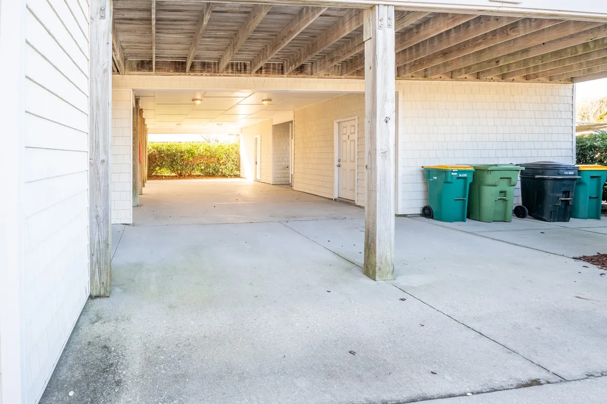 This image presents a utilitarian open space featuring a storage area and trash bins, as well as room suitable for parking vehicles or storing outdoor equipment. The space is clearly designed for practicality and easy access, ideal for active families returning from the beach or unloading gear.