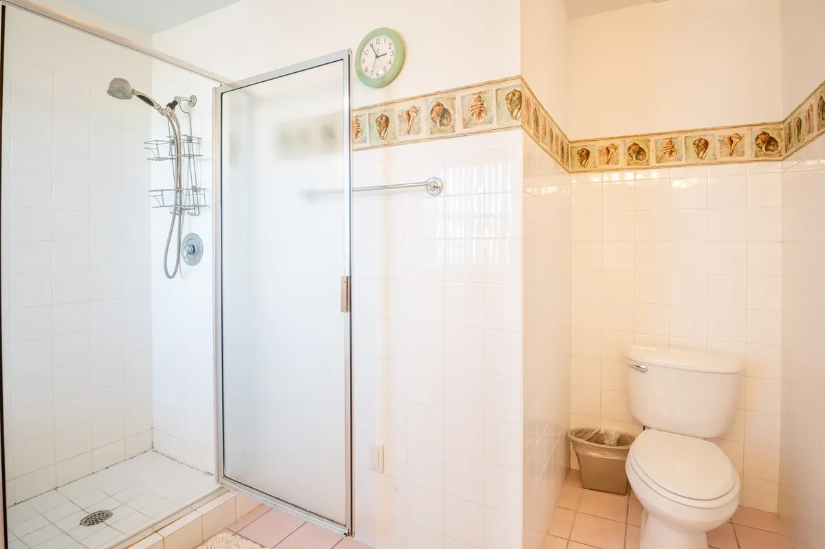 A fresh, inviting bathroom featuring a shower stall, toilet, and decorative border. The scene suggests a convenient spot for a post-beach rinse, offering a sense of relaxation and renewal after outdoor activities.