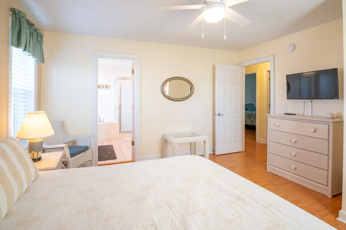 A calm and cozy bedroom featuring a bed with decorative pillows, a nightstand lamp, and a mirror on the wall. The setting suggests a relaxing space perfect for unwinding, reading, or enjoying a quiet night in.
