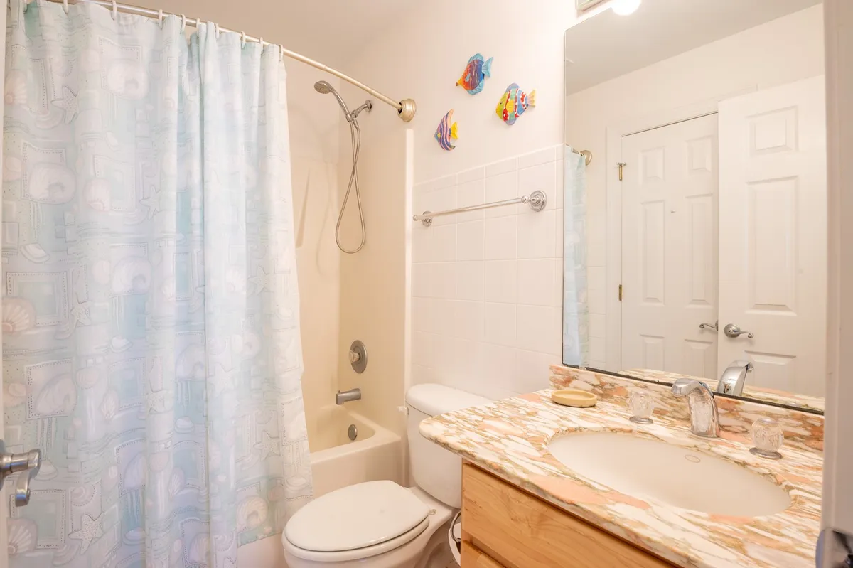 A cheerful bathroom with colorful fish decorations, a marble countertop, and a shower curtain with an aquatic motif. The playful decor evokes a coastal vibe and hints at the fun, water-centric lifestyle just outside the condo doors.